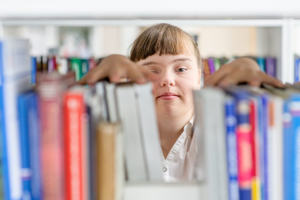 Junge Frau mit Down Syndrom sichtet Bücher in einer Bibliothek